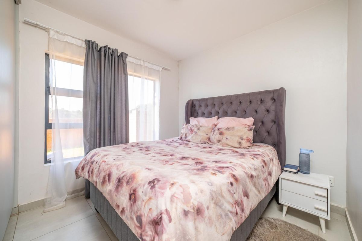 A well-lit bedroom featuring neutral tiled flooring and a large window with aluminium frames, providing a clean and functional living space.