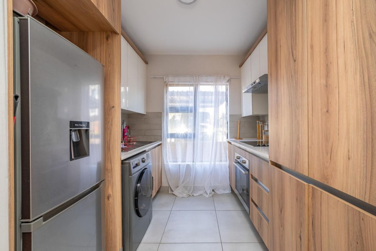 Modern galley-style kitchen featuring wood-grain cabinetry, integrated appliances, sleek tiled backsplash, and neutral floor tiles.