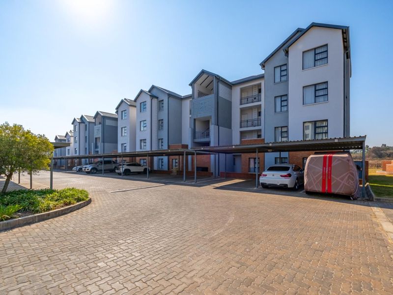 Exterior view of a multi-story apartment complex featuring paved parking areas and covered carports.