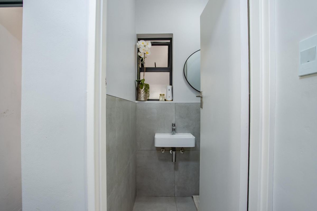 A compact, modern guest bathroom featuring a wall-mounted basin, neutral grey tiling, and a clean, minimalist aesthetic.
