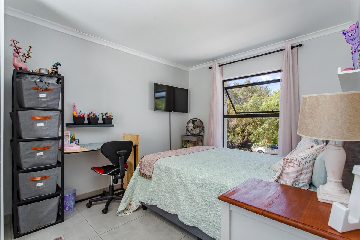 A well-maintained bedroom featuring tiled flooring, neutral wall finishes, and an awning window providing natural light and garden views.