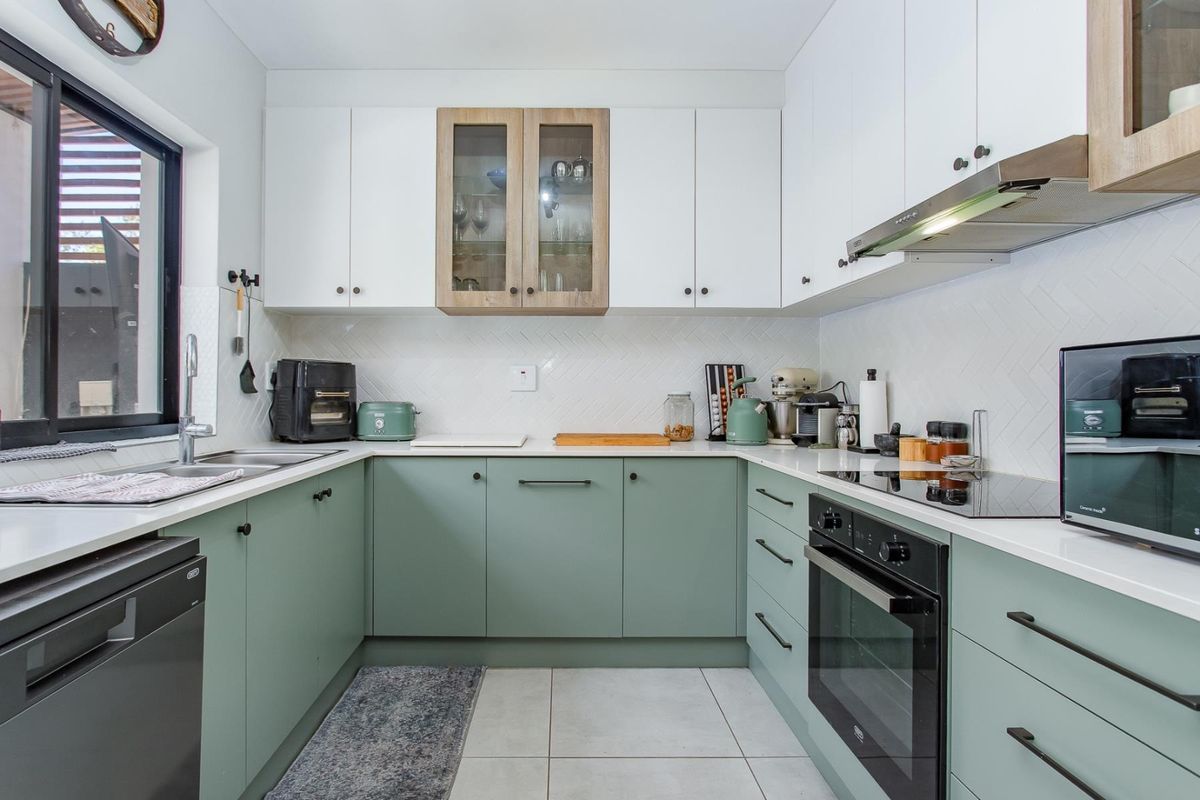 Modern U-shaped kitchen featuring sage green lower cabinets, white upper cabinetry, stone countertops, herringbone backsplash, and integrated stainless steel appliances.