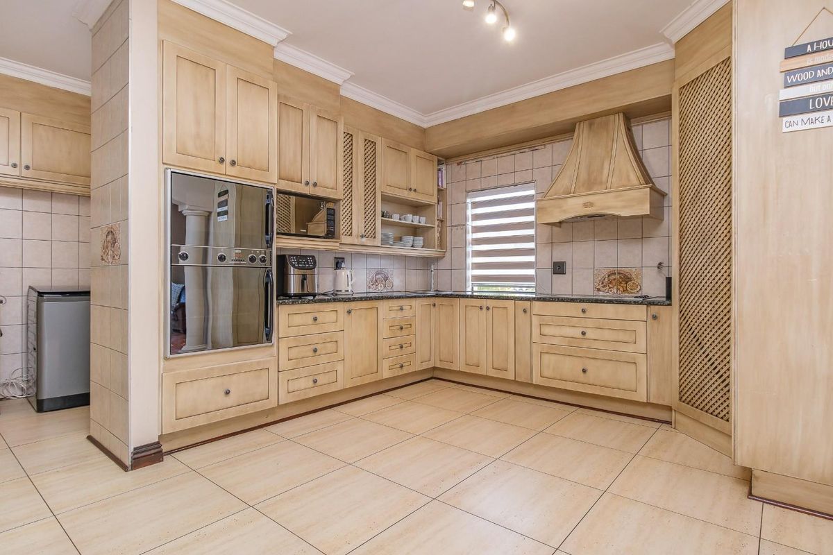 A functional kitchen featuring light wood cabinetry, granite countertops, built-in oven, extractor fan, and tiled flooring with a neutral backsplash.