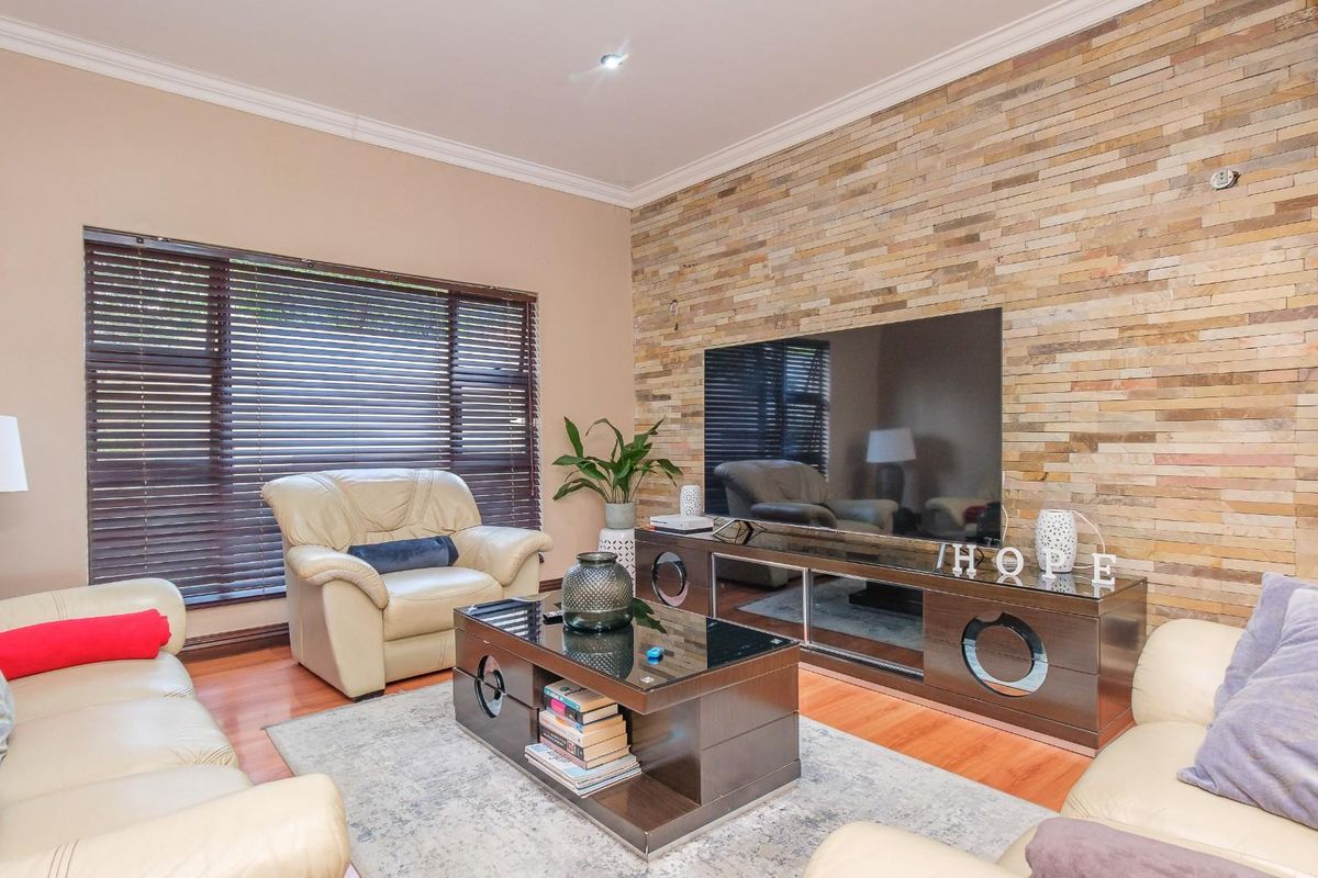 A comfortable living room featuring a prominent stacked stone accent wall, warm laminate flooring, and large windows fitted with venetian blinds.