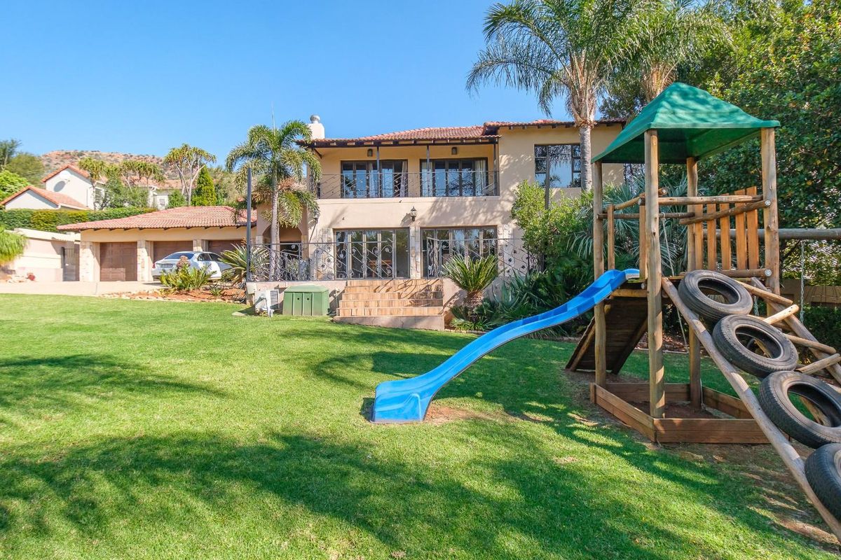 Spacious rear garden featuring a well-maintained lawn, paved patio area, and a two-story residence with a balcony and attached double garage.