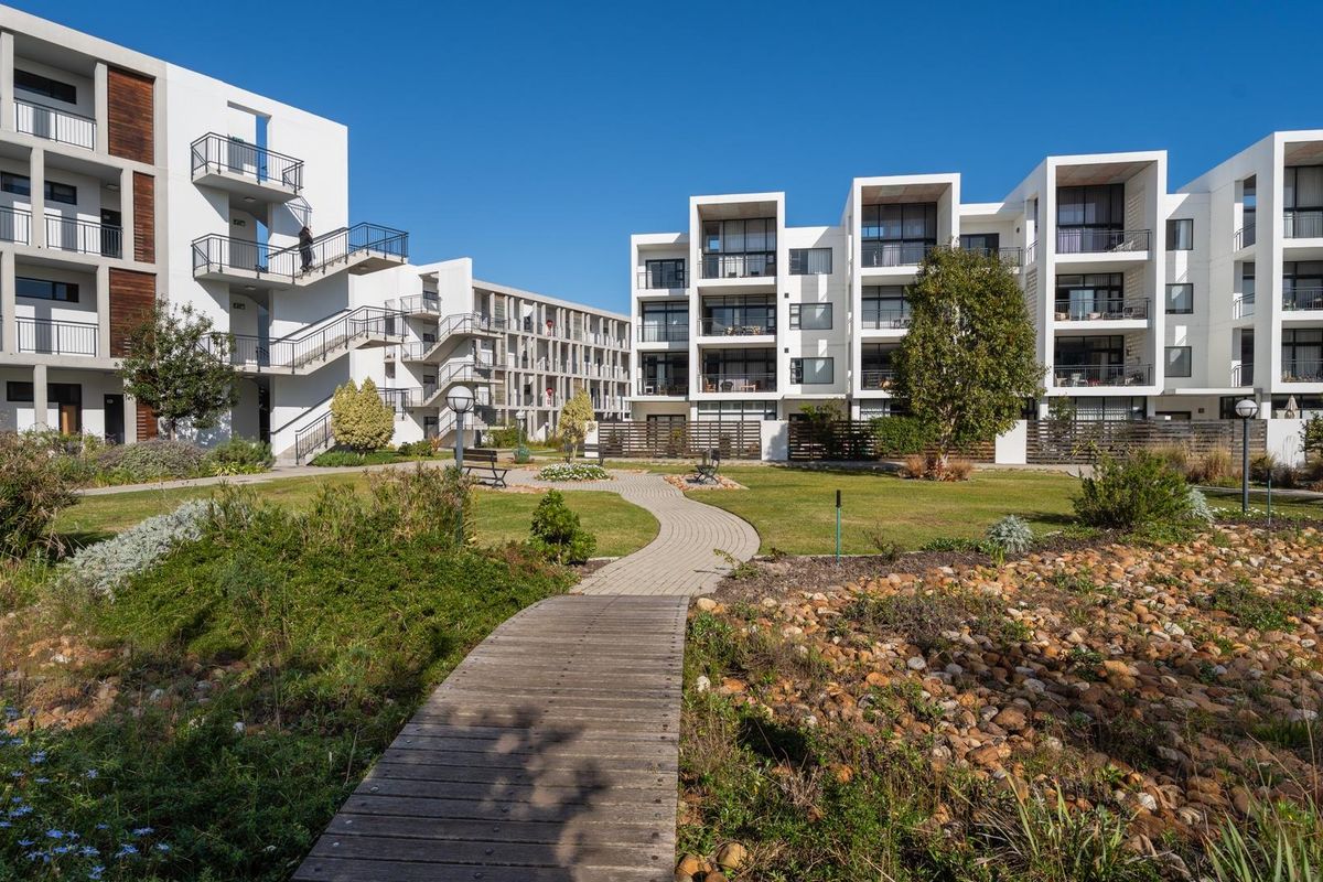 A well-maintained apartment complex featuring landscaped gardens, paved pathways, wooden boardwalks, and modern building facades with private balconies.