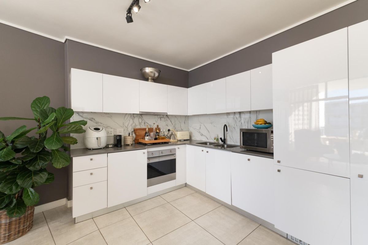 Modern kitchen featuring white gloss cabinetry, marble-look splashback, built-in oven, and sleek black fixtures, complemented by neutral tiled flooring and contemporary track lighting.
