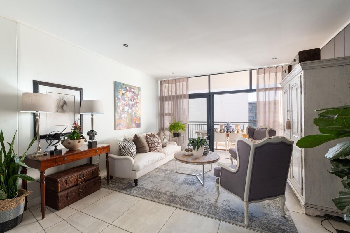 A bright and well-maintained living room featuring tiled flooring, recessed lighting, and large sliding glass doors providing access to the balcony.