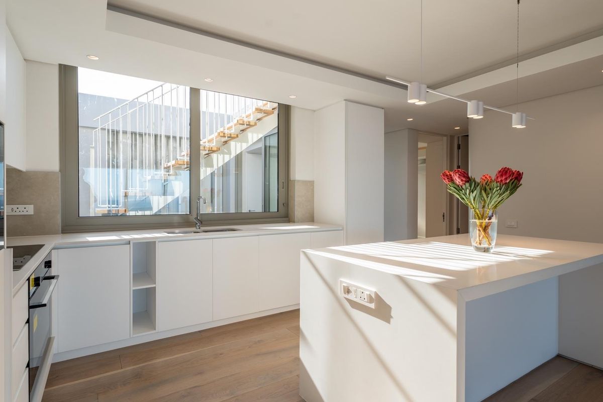 Modern, minimalist kitchen featuring a central island, handleless white cabinetry, integrated appliances, and high-quality hardwood flooring with abundant natural light.