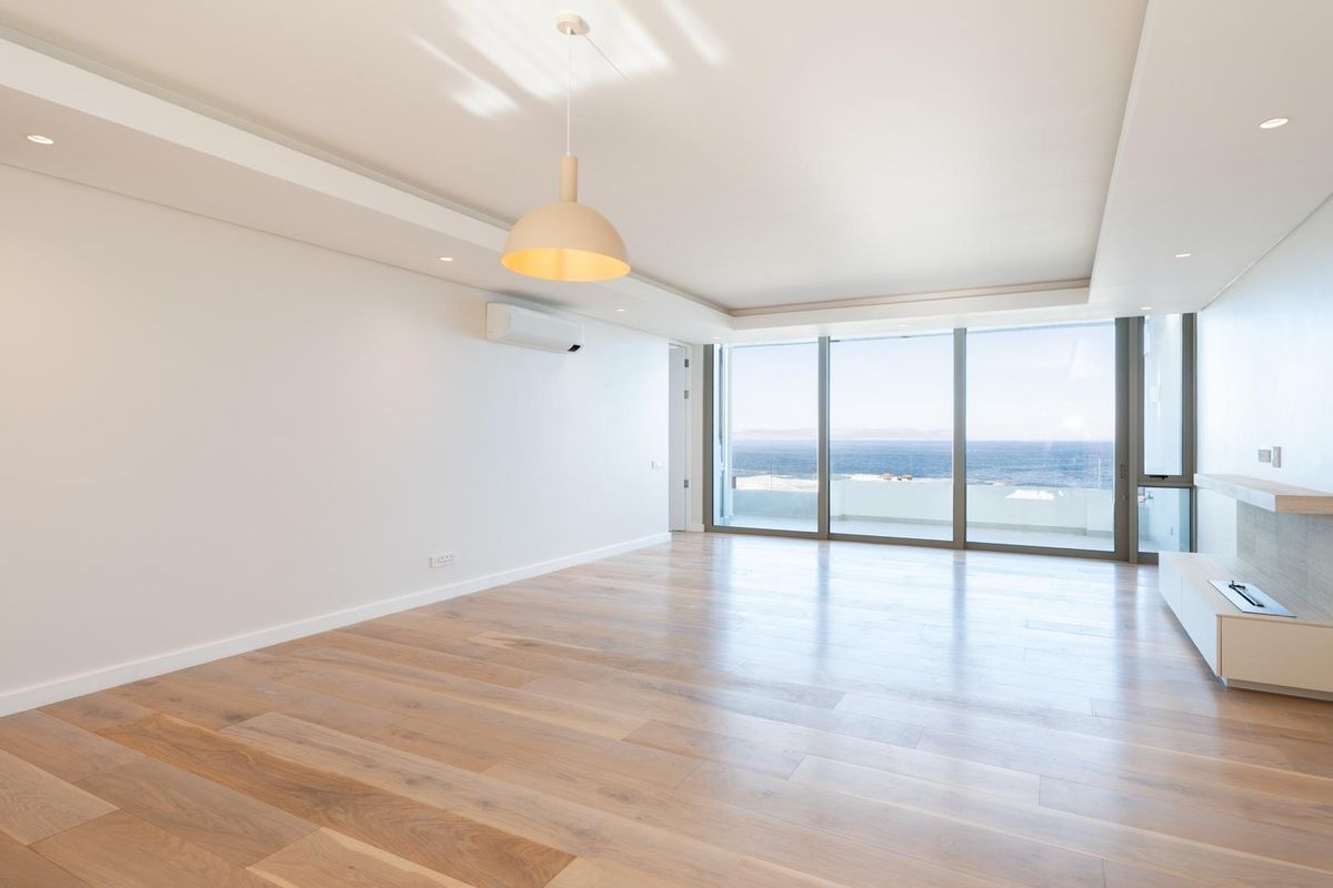 Spacious, light-filled living area featuring premium hardwood flooring, a built-in fireplace, and floor-to-ceiling glass doors offering expansive ocean views.