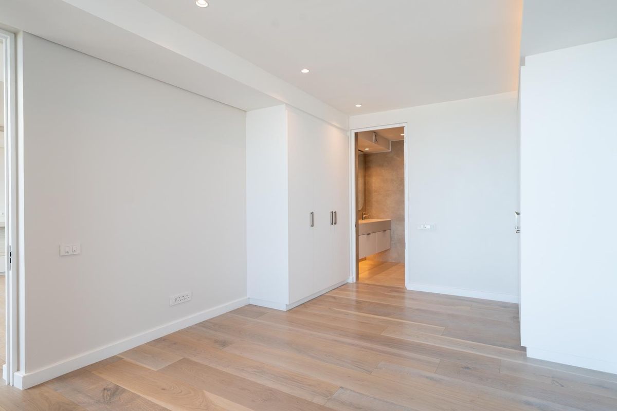 A bright, modern bedroom featuring light hardwood flooring, built-in storage, and direct access to an en-suite bathroom.