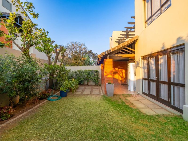 A private rear garden featuring a small lawn, paved pathway, and a covered patio area with brick pillars and a timber pergola structure.