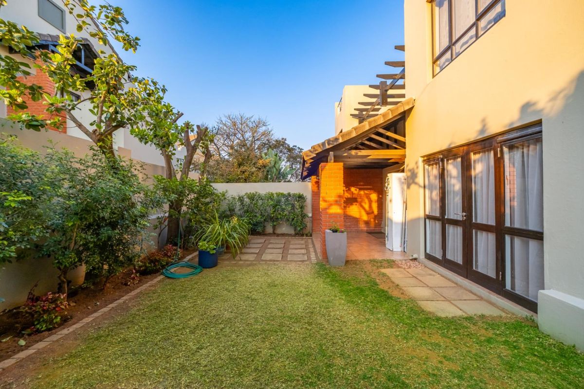 A private rear garden featuring a small lawn, paved pathway, and a covered patio area with brick pillars and a timber pergola structure.