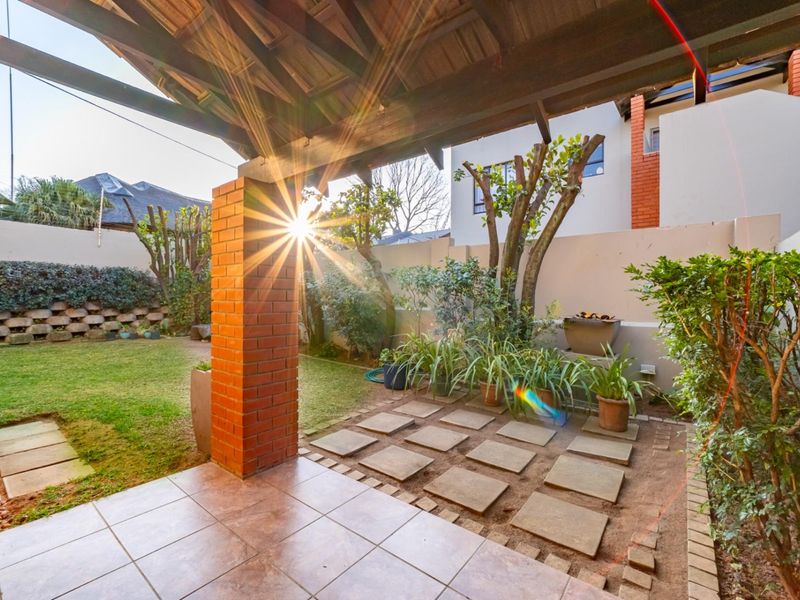 A covered patio area featuring a tiled floor and exposed timber roof structure, overlooking a private garden with a brick retaining wall.