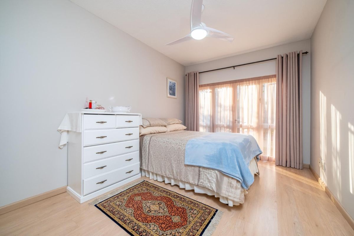 A well-maintained bedroom featuring light-toned laminate flooring, a modern ceiling fan, and a sliding glass door providing natural light.
