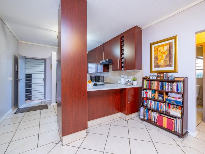 A functional kitchen featuring dark wood cabinetry, tiled flooring, and a breakfast counter, with an adjacent entrance area and security gate.