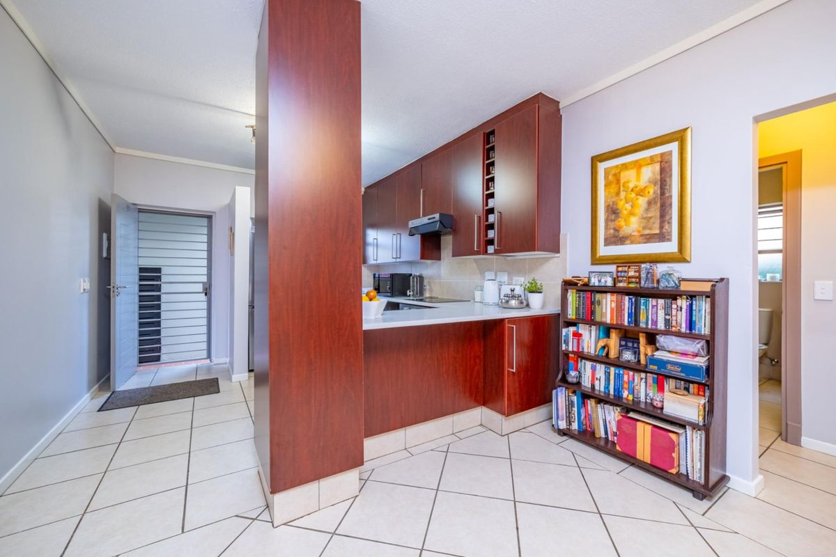 A functional kitchen featuring dark wood cabinetry, tiled flooring, and a breakfast counter, with an adjacent entrance area and security gate.