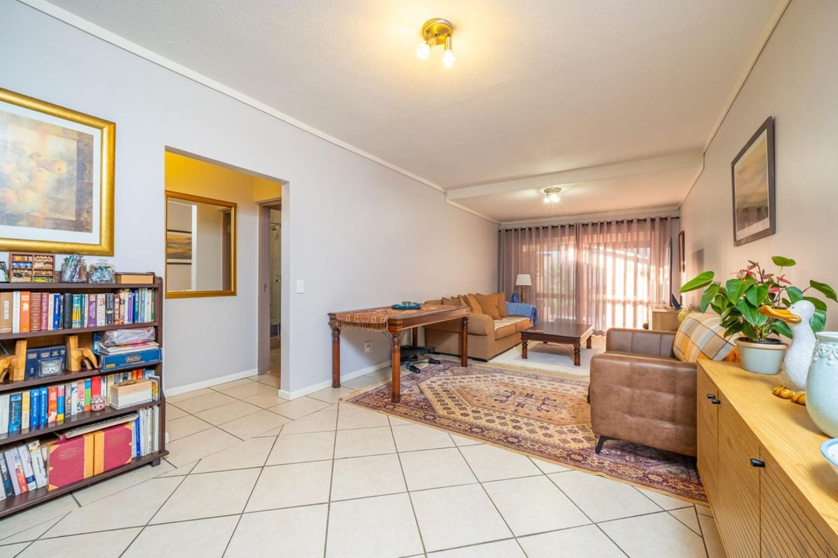 Spacious living room featuring neutral tiled flooring, ample natural light from sliding glass doors, and direct access to an adjacent hallway.