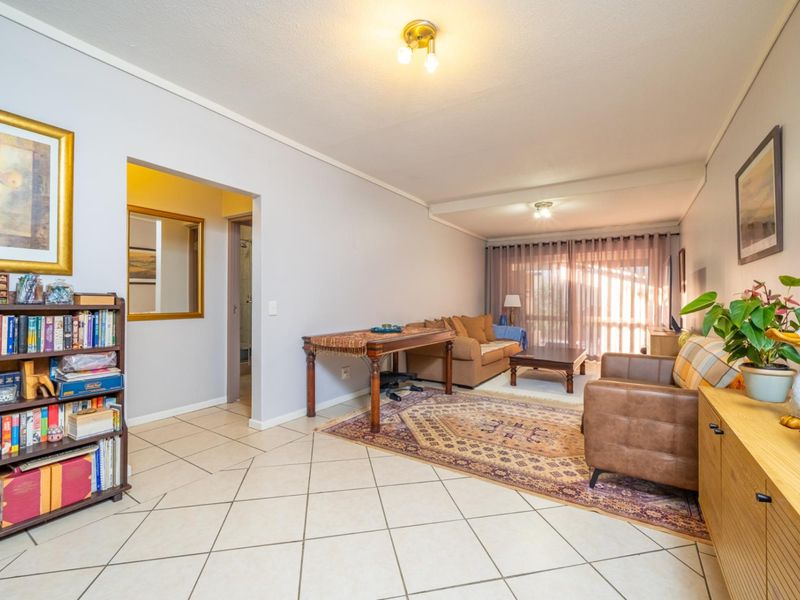 Spacious living room featuring neutral tiled flooring, ample natural light from sliding glass doors, and direct access to an adjacent hallway.