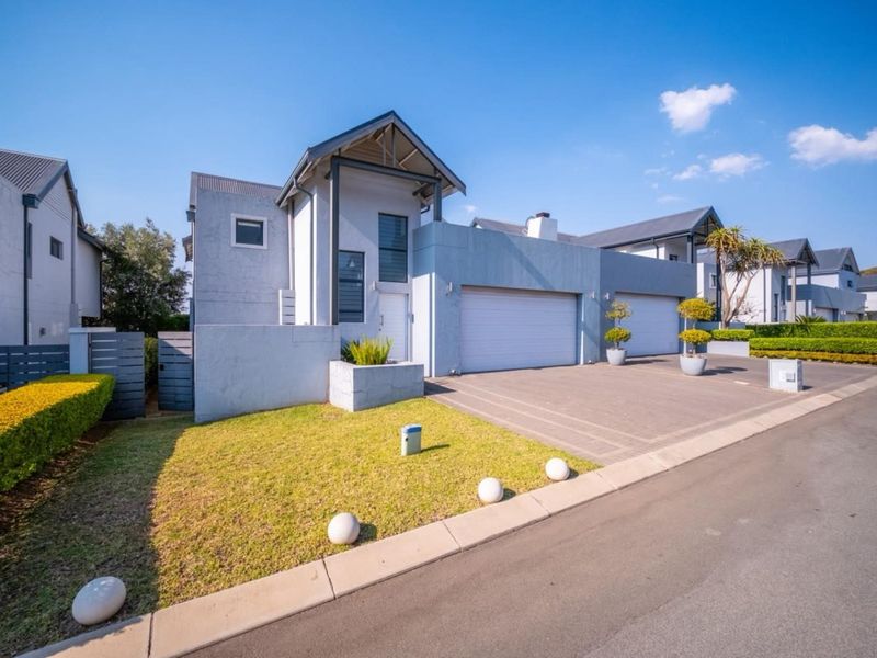 Modern townhouse exterior featuring a double garage, paved driveway, and well-maintained front lawn with contemporary architectural design.