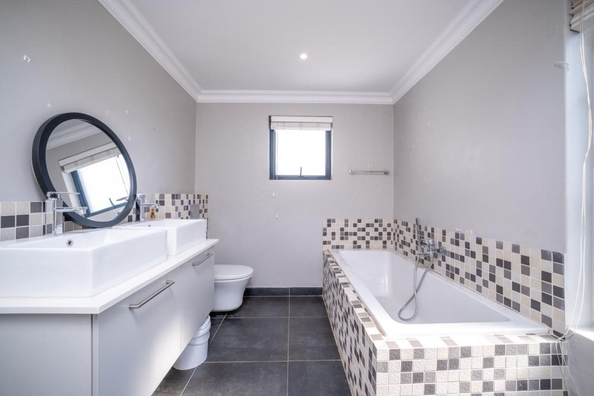 Modern bathroom featuring a double vanity, built-in bathtub with mosaic tile surround, dark floor tiles, and neutral wall finishes.
