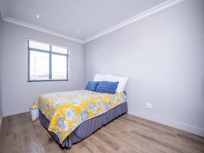 A well-maintained bedroom featuring modern laminate flooring, built-in cupboards, recessed downlights, and neutral wall finishes with classic cornicing.