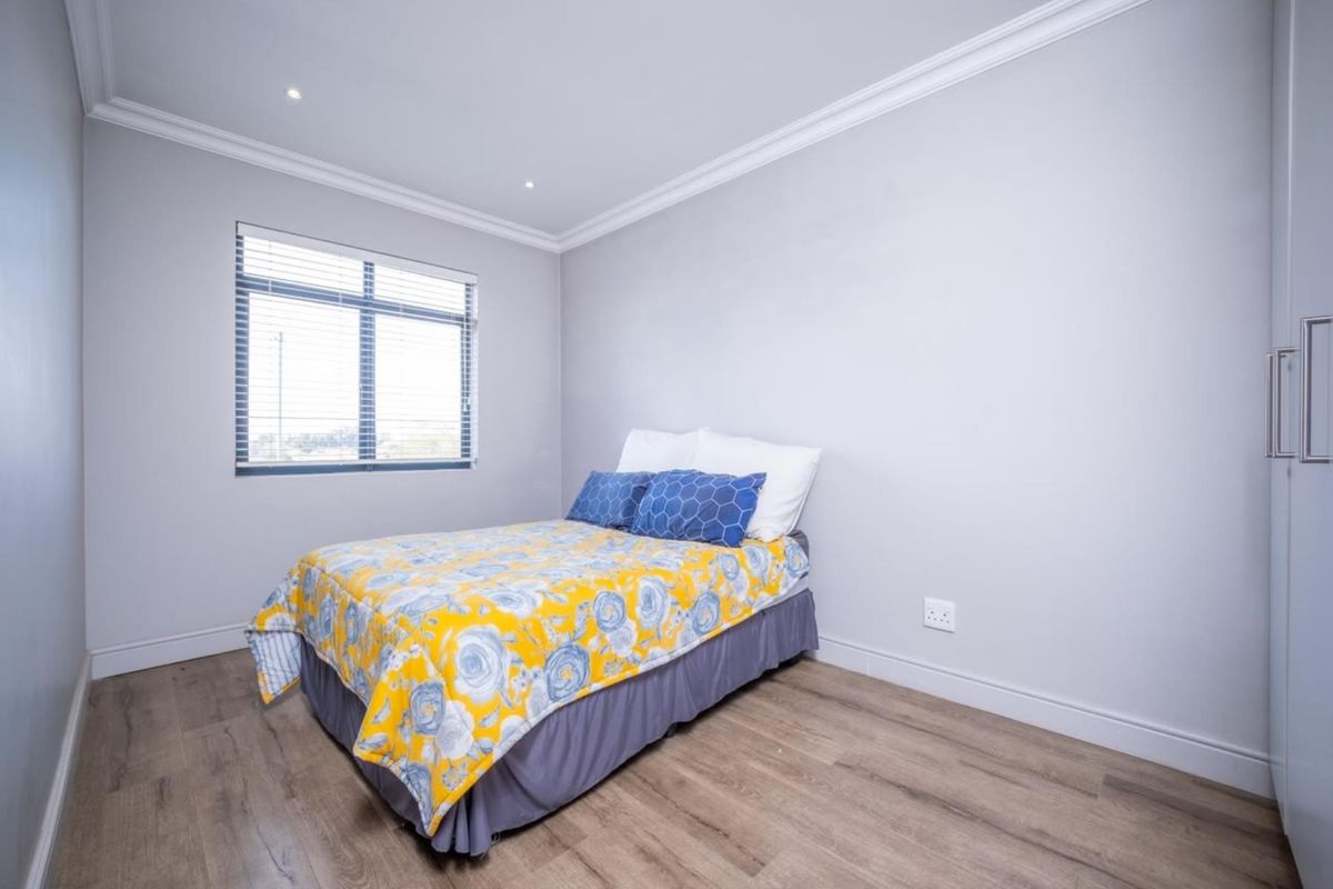 A well-maintained bedroom featuring modern laminate flooring, built-in cupboards, recessed downlights, and neutral wall finishes with classic cornicing.