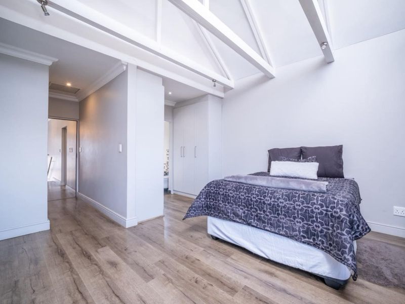 Spacious bedroom featuring high vaulted ceilings with exposed rafters, modern laminate flooring, and convenient built-in cupboard storage.