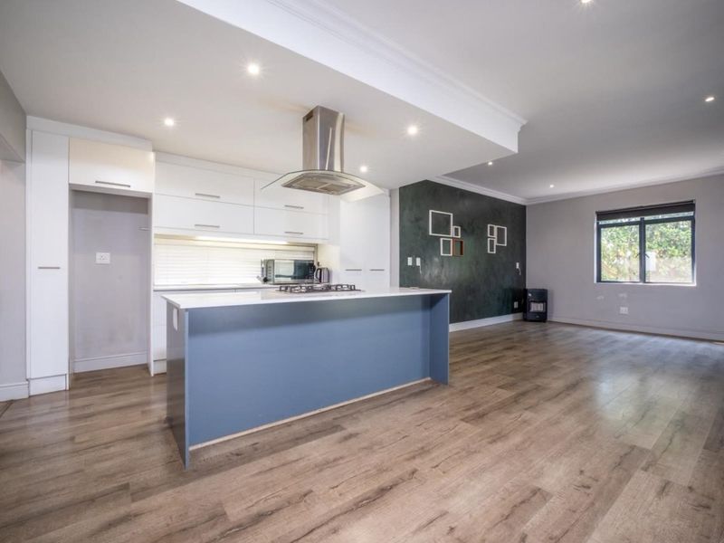 Spacious open-plan living area featuring a modern kitchen with a central island, gas hob, extractor fan, and sleek cabinetry, finished with laminate flooring.