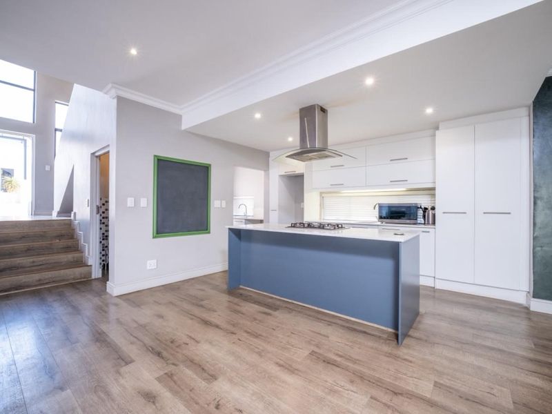 Modern open-plan kitchen featuring a central island with gas cooktop, sleek white cabinetry, and high-quality laminate flooring, seamlessly connected to the staircase area.
