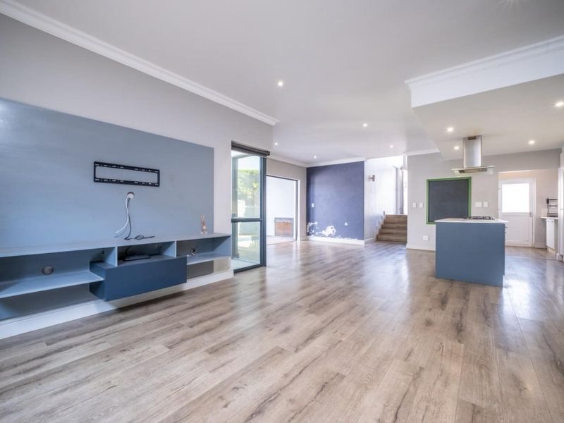 Spacious open-plan living and kitchen area featuring laminate flooring, a built-in media console, and a central kitchen island with an extractor fan.