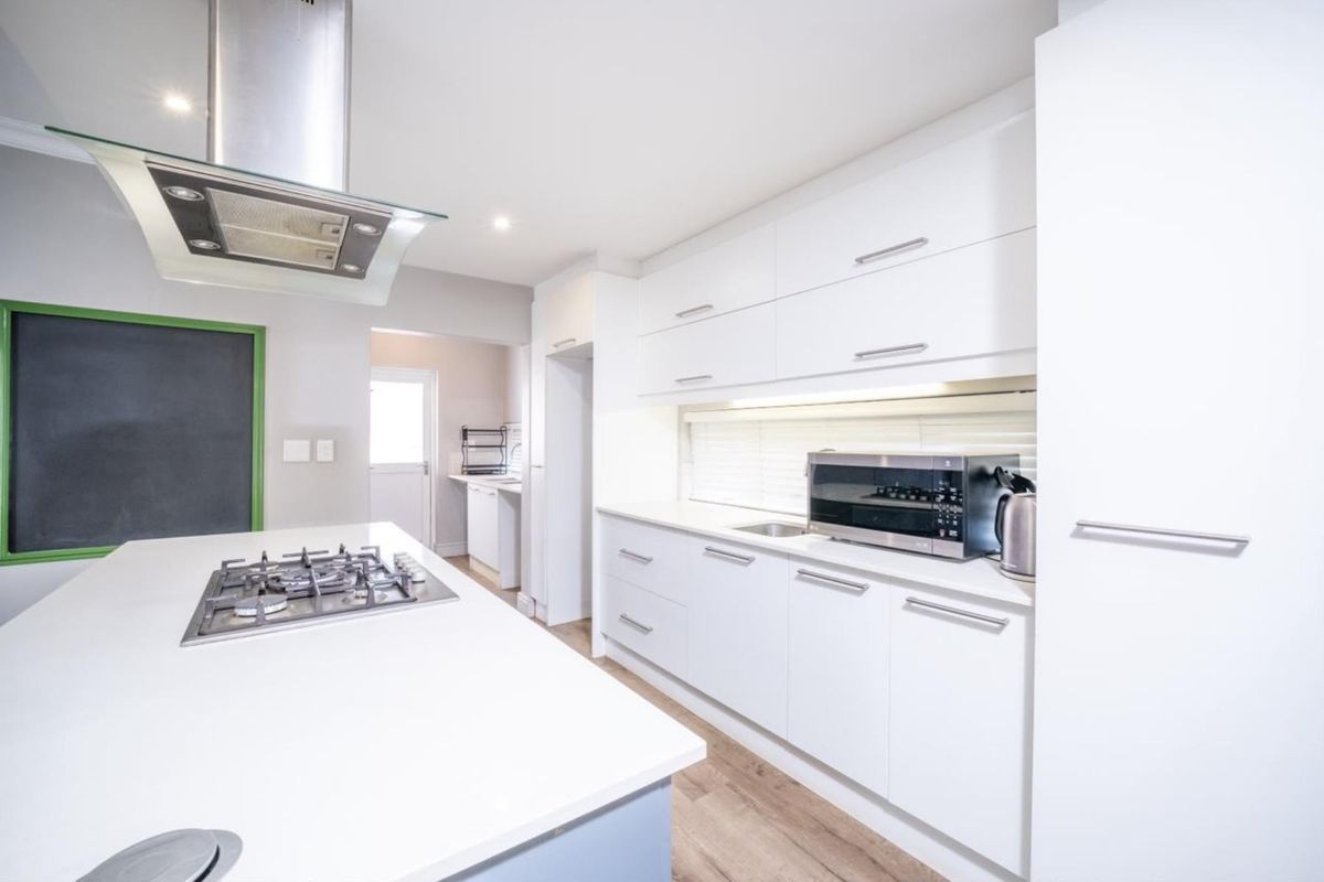 Modern kitchen featuring a central island with a gas cooktop, sleek white cabinetry, stainless steel extractor fan, and durable laminate flooring.
