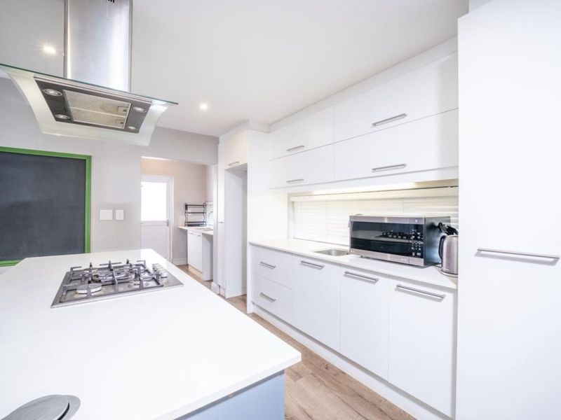 Modern kitchen featuring a central island with a gas cooktop, sleek white cabinetry, stainless steel extractor fan, and durable laminate flooring.