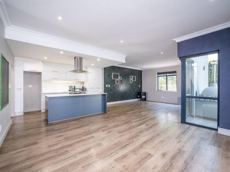 Spacious open-plan living area featuring a modern kitchen with a central island, sleek cabinetry, and durable laminate flooring, leading to an outdoor patio space.