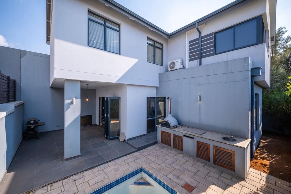 Rear exterior view featuring a covered patio, built-in outdoor kitchen with pizza oven, and a swimming pool.