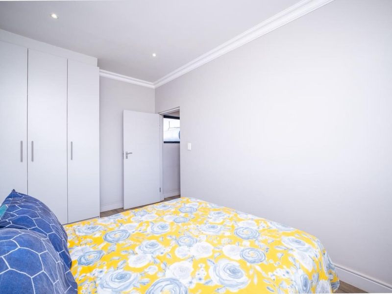 A clean, well-maintained bedroom featuring built-in cupboards, recessed downlighting, and modern laminate flooring with neutral wall finishes.