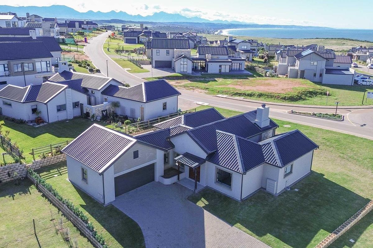 Aerial view of a modern residential property featuring a metal roof, paved driveway, double garage, and well-maintained lawn within a coastal estate.
