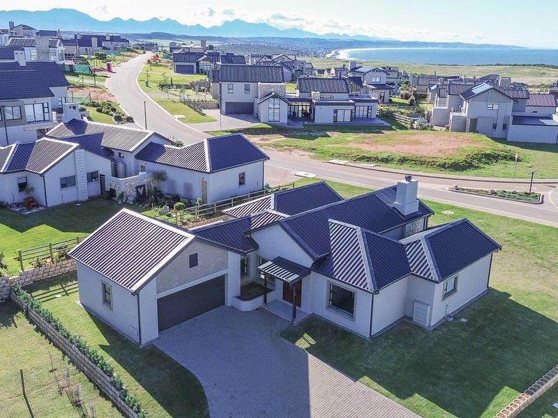 Aerial view of a modern residential property featuring a metal roof, paved driveway, double garage, and well-maintained lawn within a coastal estate.