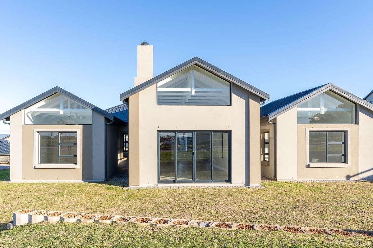 A modern rear elevation of a house featuring a symmetrical design, metal roofing, large glass sliding doors, and expansive windows set against a clear sky.