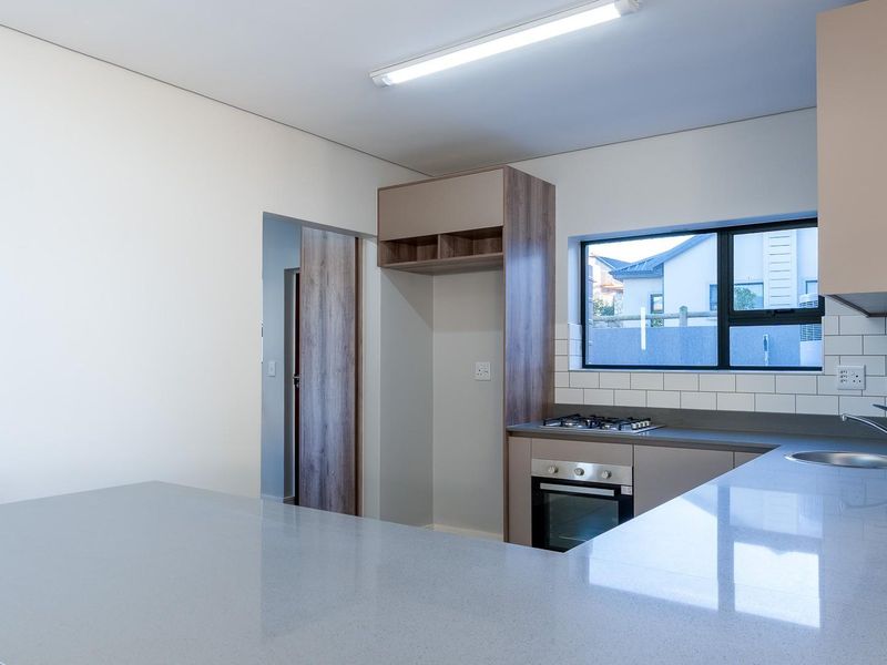 Modern, clean-lined kitchen featuring quartz countertops, subway tile backsplash, built-in oven, gas hob, and ample cabinetry in a neutral, contemporary finish.