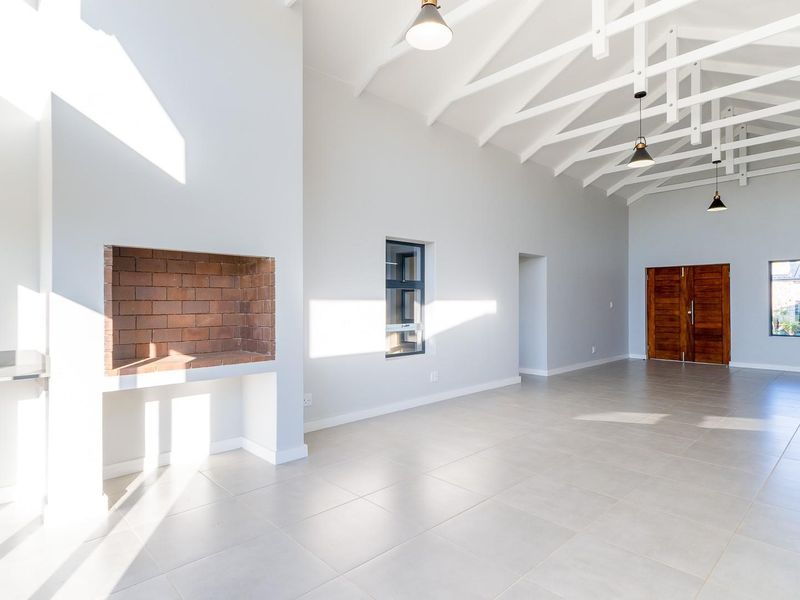 Spacious open-plan living area featuring high vaulted ceilings with exposed white trusses, tiled floors, and a built-in brick fireplace.