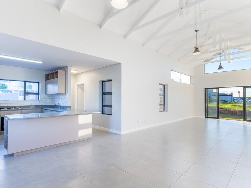 Spacious open-plan living area featuring a modern kitchen with island, vaulted ceilings with exposed trusses, and large sliding doors leading to the exterior.