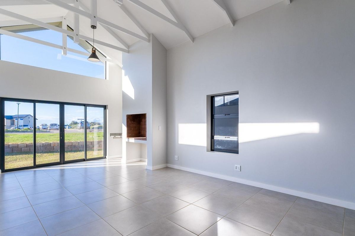 Spacious open-plan living area featuring high vaulted ceilings with exposed trusses, tiled floors, a built-in fireplace, and large sliding doors leading to the exterior.