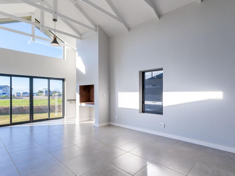 Spacious open-plan living area featuring high vaulted ceilings with exposed trusses, tiled floors, a built-in fireplace, and large sliding doors leading to the exterior.