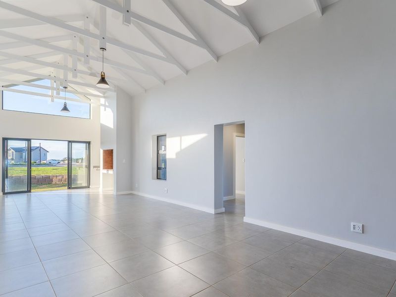 Spacious open-plan living area featuring high vaulted ceilings with exposed white trusses, large sliding glass doors, and modern neutral tiled flooring.