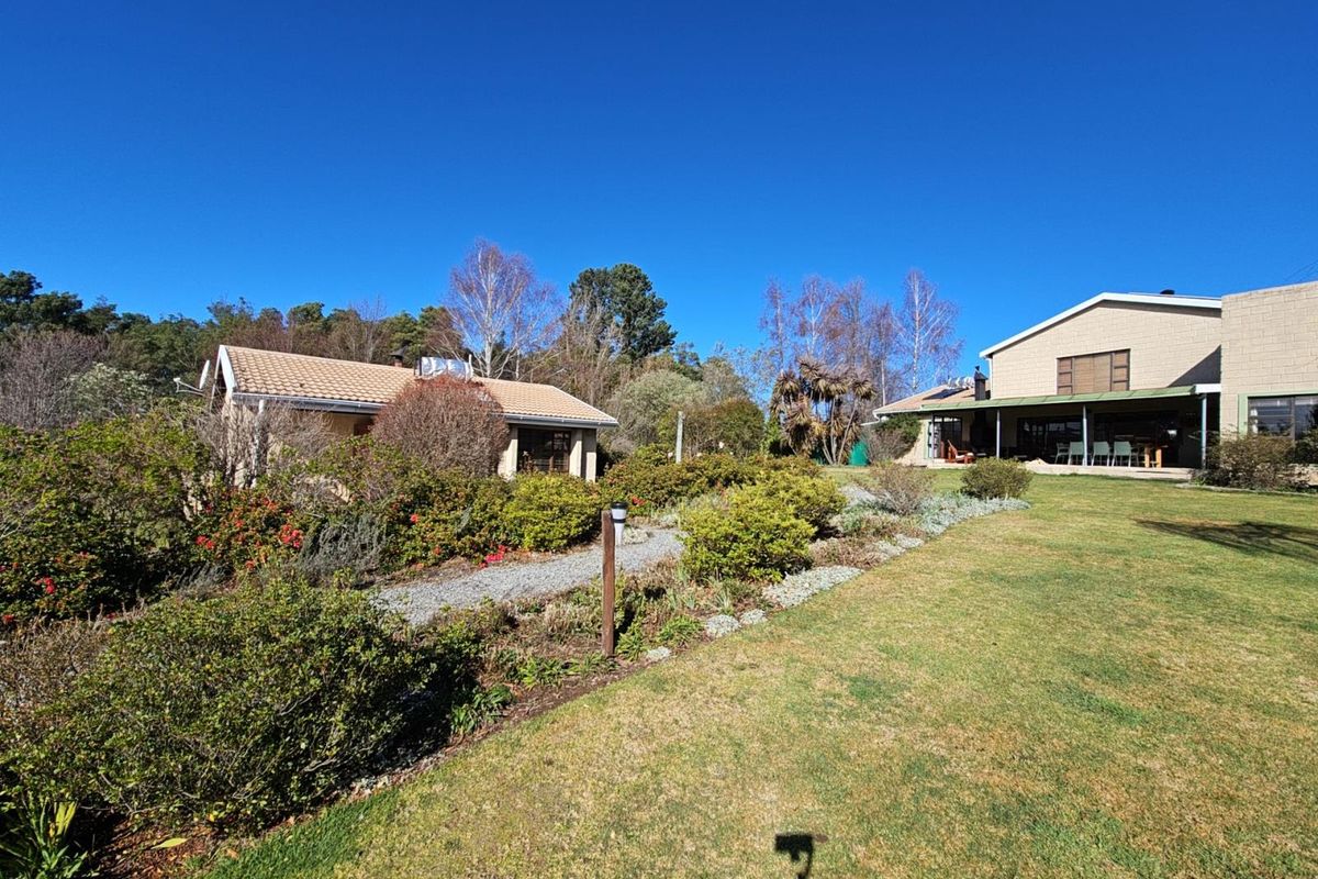 A spacious rear garden featuring a gravel pathway, landscaped shrubbery, and a covered patio area attached to the main residence.