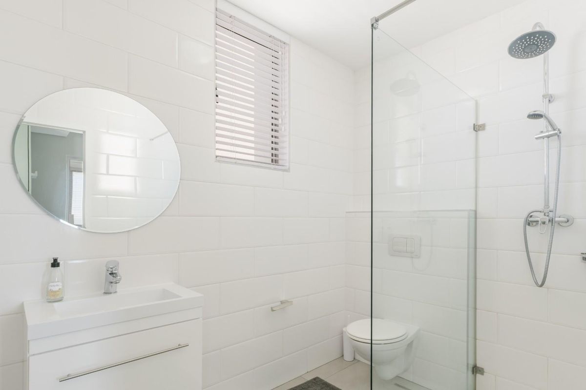 Modern bathroom featuring white subway wall tiles, a wall-mounted vanity with basin, a wall-hung toilet, and a glass-enclosed shower with rainfall shower head.