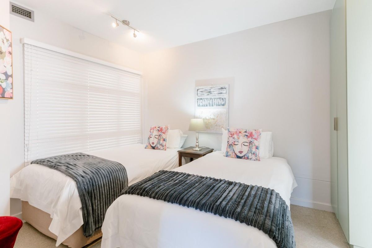A well-maintained bedroom featuring neutral walls, built-in wardrobe storage, adjustable venetian blinds, and modern track lighting.