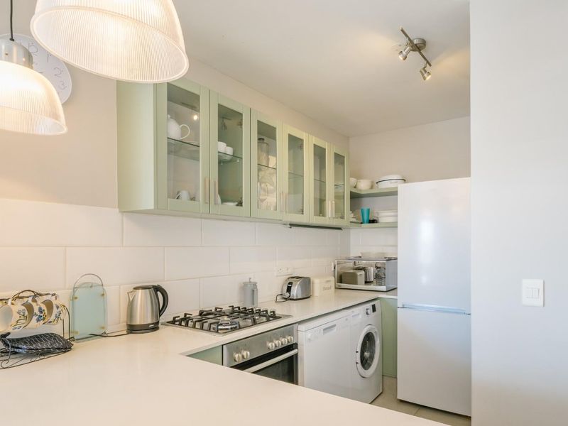 A well-maintained kitchen featuring light green cabinetry, subway tile backsplash, gas hob, built-in oven, and integrated laundry appliances.