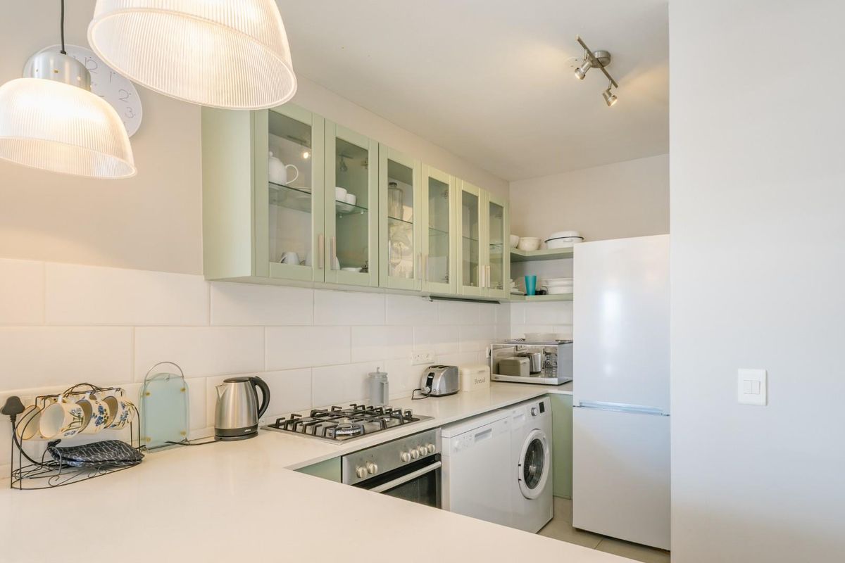 A well-maintained kitchen featuring light green cabinetry, subway tile backsplash, gas hob, built-in oven, and integrated laundry appliances.